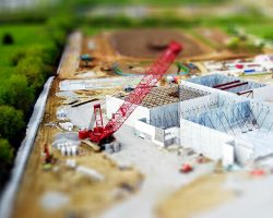 Aerial view of a construction site with a red crane amidst green fields and concrete buildings.